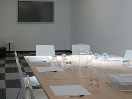 Un salón de conferencias con una larga mesa, sillas, una pizarra y diversos objetos como vasos y una jarra de agua.
