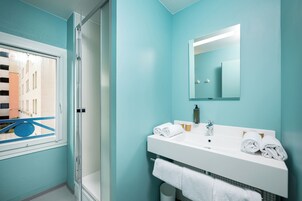 Un baño con un lavamanos blanco, dos toallas, un espejo y una ventana con vistas a edificios.