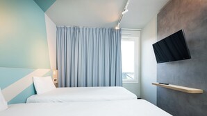 A modern hotel room with a large bed, a mounted TV, and a window with curtains. - ibis budget Lyon Caluire Cite Internationale (Caluire-et-Cuire)