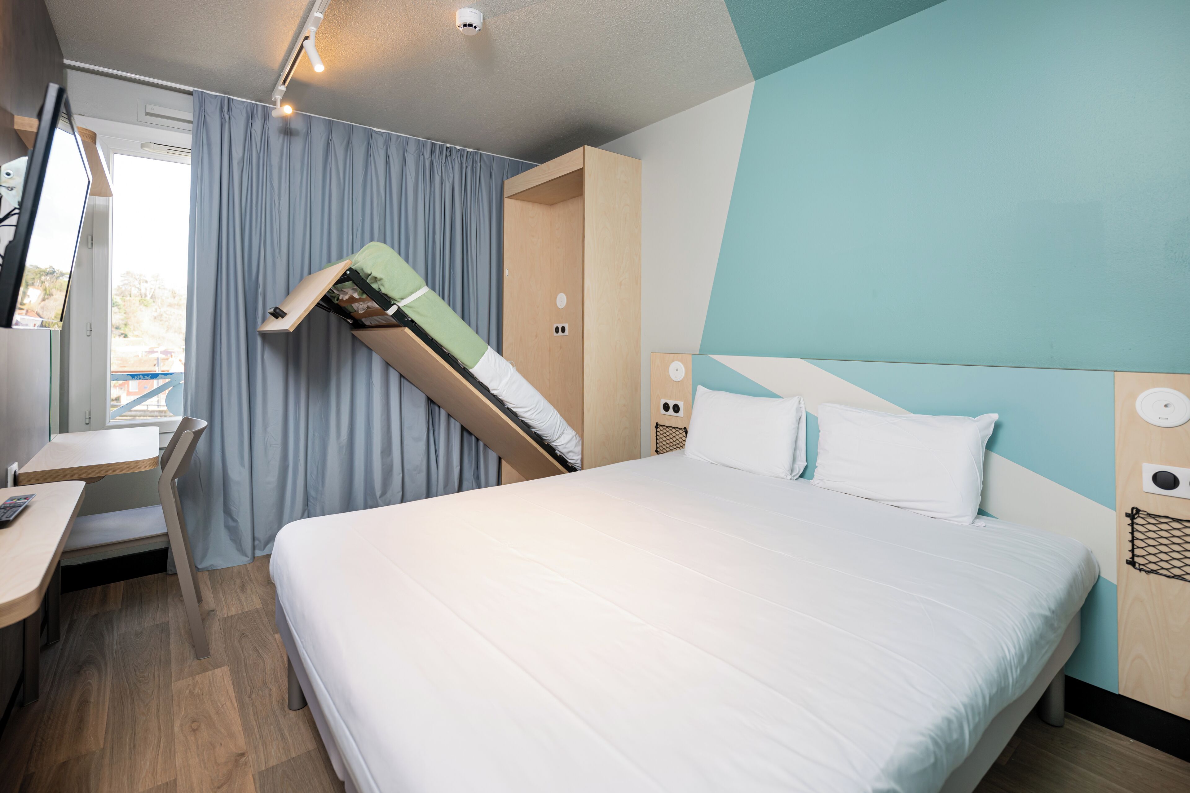A modern hotel room with a bed, a desk, and a built-in wardrobe.