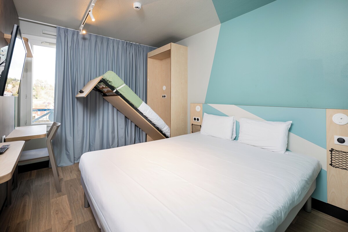 A modern hotel room with a bed, a desk, and a built-in wardrobe.