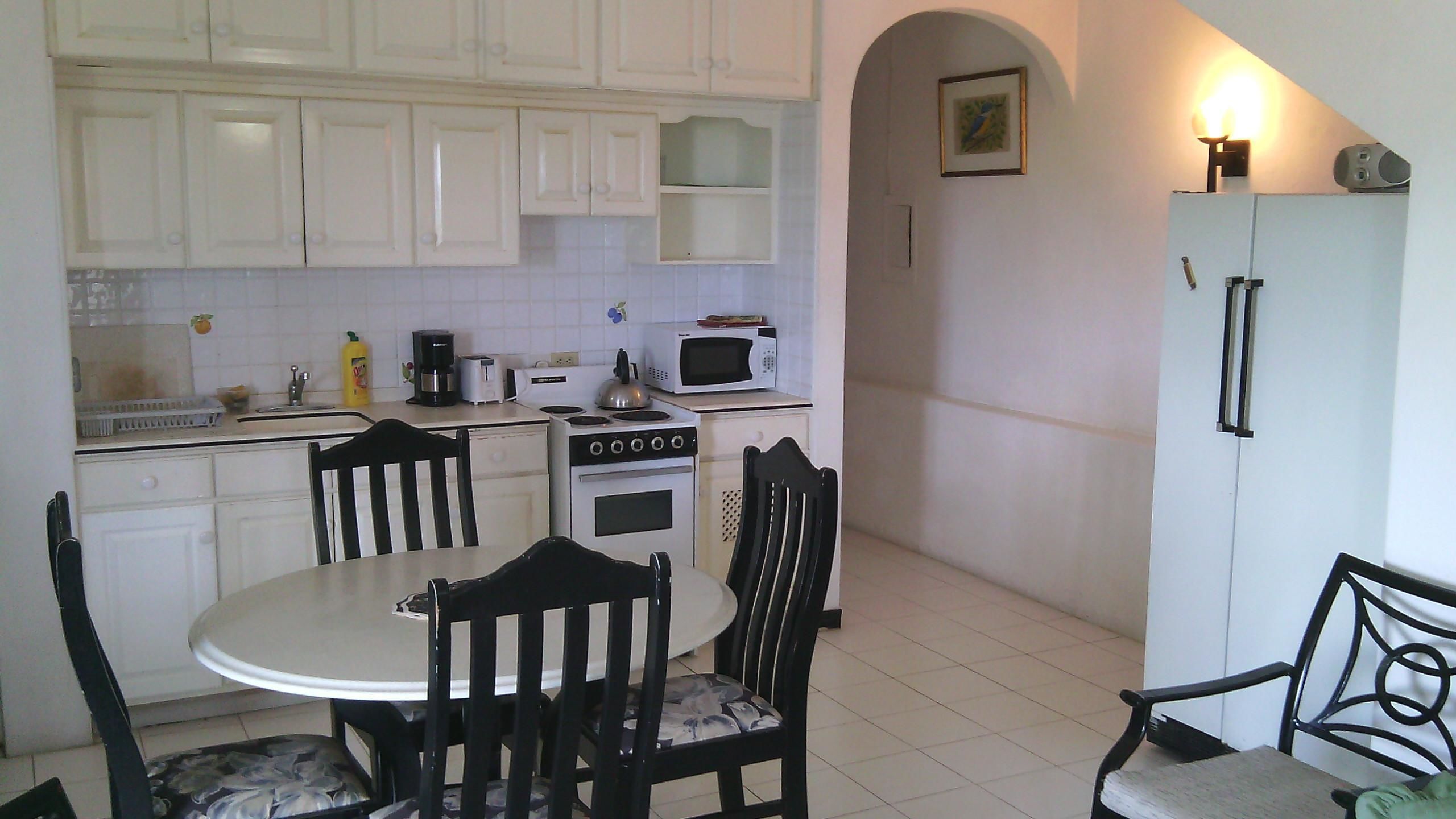 A compact kitchen with white cabinets, a stove, a microwave, and a dining table with chairs.