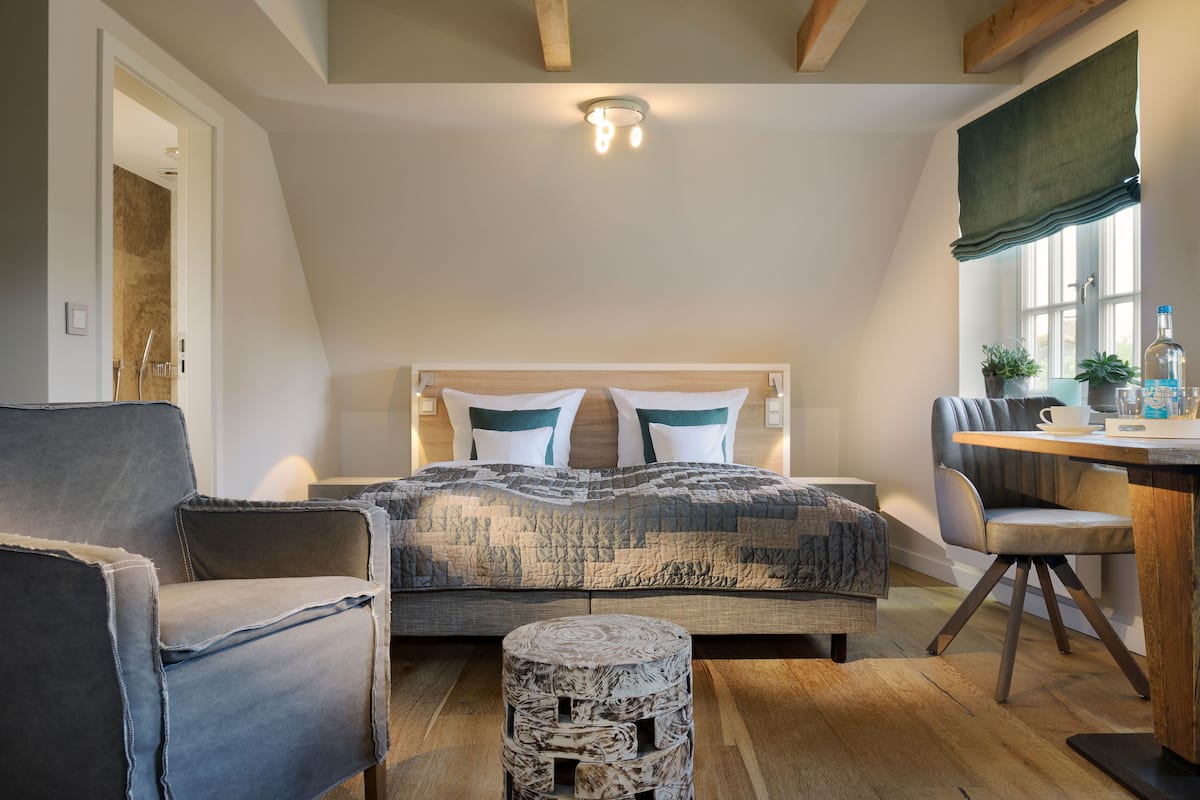 Ein Schlafzimmer mit Bett, Sessel, kleinem Tisch und Fenster mit Aussicht.