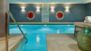 Ein Schwimmbecken mit Metallgeländer, zwei Wandleuchten und einer Sitzgelegenheit mit einem Korbstuhl und einem runden Tisch.
