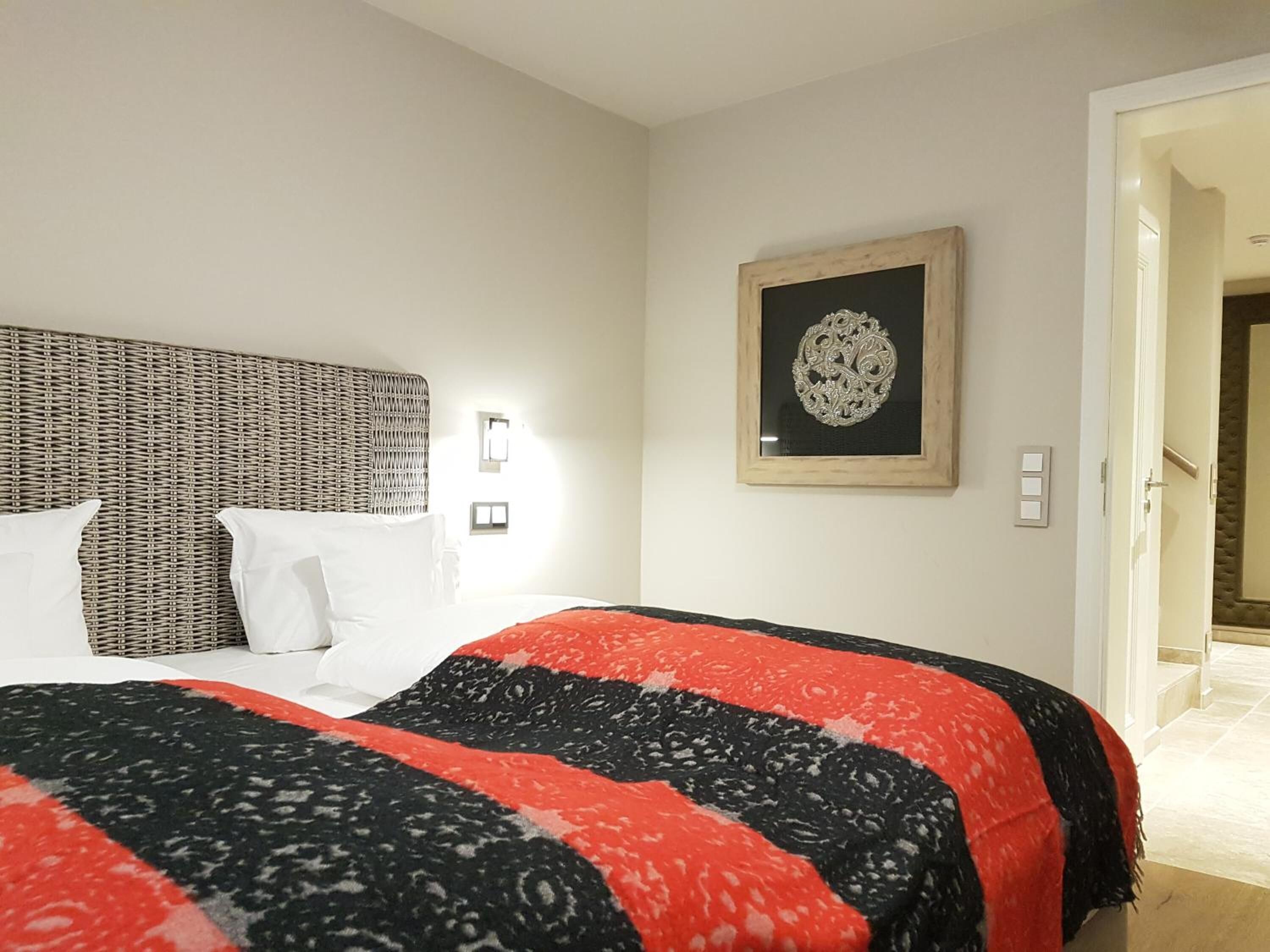Une chambre d’hôtel avec un grand lit, une tête de lit en osier, une œuvre d’art encadrée au mur et une porte donnant sur une autre pièce.