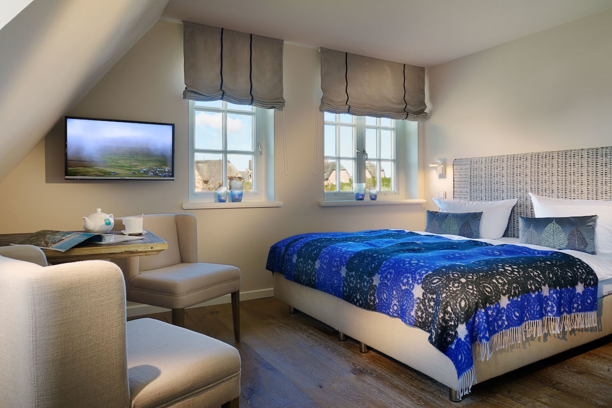 Ein Schlafzimmer mit einem Bett, einem Fernseher, einem Fenster mit Vorhängen und einem kleinen Tisch mit einem Teekännchen.