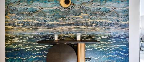 Un interior moderno con un mural texturizado, una mesa redonda negra y un pilar dorado.