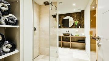 A modern bathroom with a glass shower enclosure, a round mirror, and a vanity with a bowl sink.