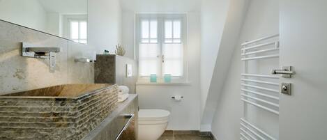 Et moderne badeværelse med en marmorvask, toilet, et vindue med persienner og en hvid radiator.