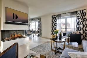 A modern living room with a fireplace, a dining area, and a sofa. - Hotel Duene (Sylt)