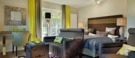 A hotel room with a bed, two armchairs, a desk, and a patterned rug.