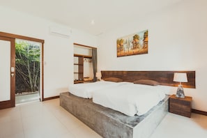 Un dormitorio con una cama grande, una mesita de noche, un cuadro y vistas al verdor a través de una puerta.