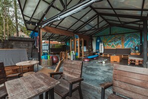 An outdoor seating area with wooden furniture and a mural on the wall. - Big Brother Surf Inn (Tibubeneng)