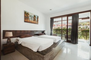 A bedroom with two beds, a wooden headboard, a nightstand with a lamp, and a painting on the wall. - Big Brother Surf Inn (Tibubeneng)