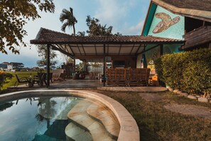 A pool area with a covered patio, a mural on the building, and outdoor furniture. - Big Brother Surf Inn (Tibubeneng)