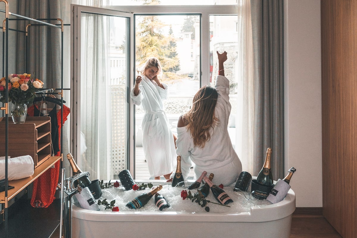 A room with a bathtub filled with champagne bottles and ice, a guitar, and a mirror reflecting a person in a robe.