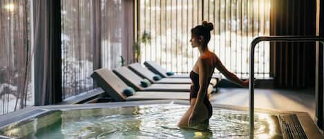 A person in a hot tub with a view of lounge chairs and a windowed wall.