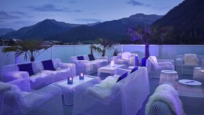 A rooftop terrace with wicker furniture and a view of mountains. - Hard Rock Hotel Davos (Davos)