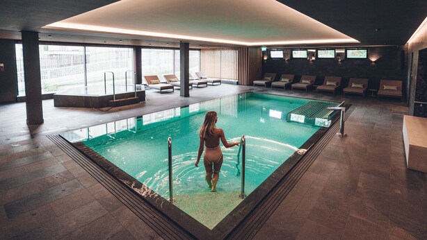 A modern indoor swimming pool with a clear view of the pool area, a lounge with chairs, and a view of the outside. - Hard Rock Hotel Davos (Davos)