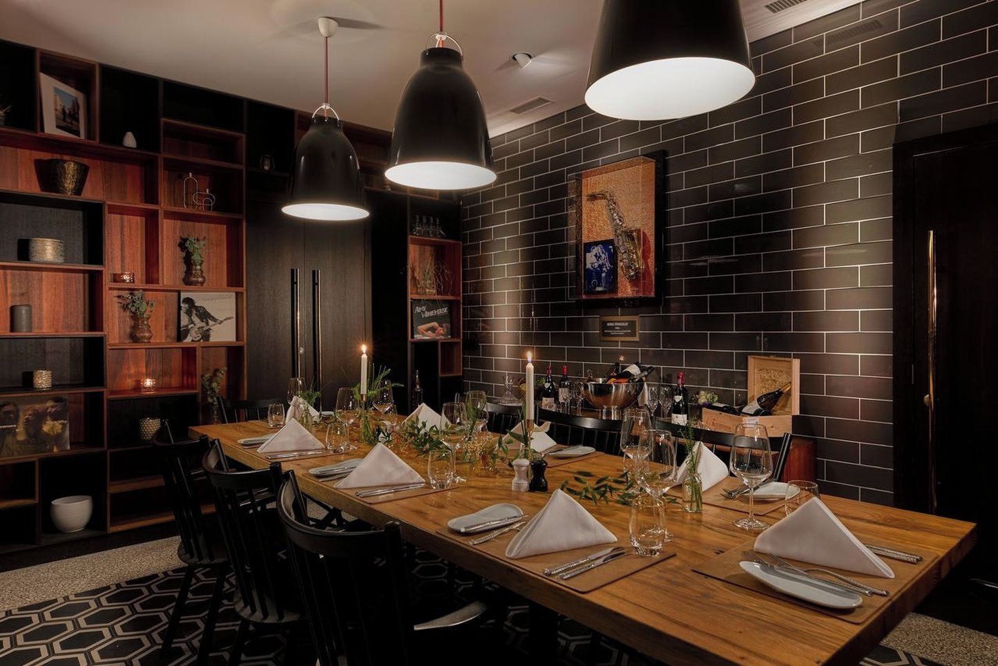 Comedor con una mesa de madera alargada dispuesta para seis personas, rodeada de sillas negras y con iluminación colgante.