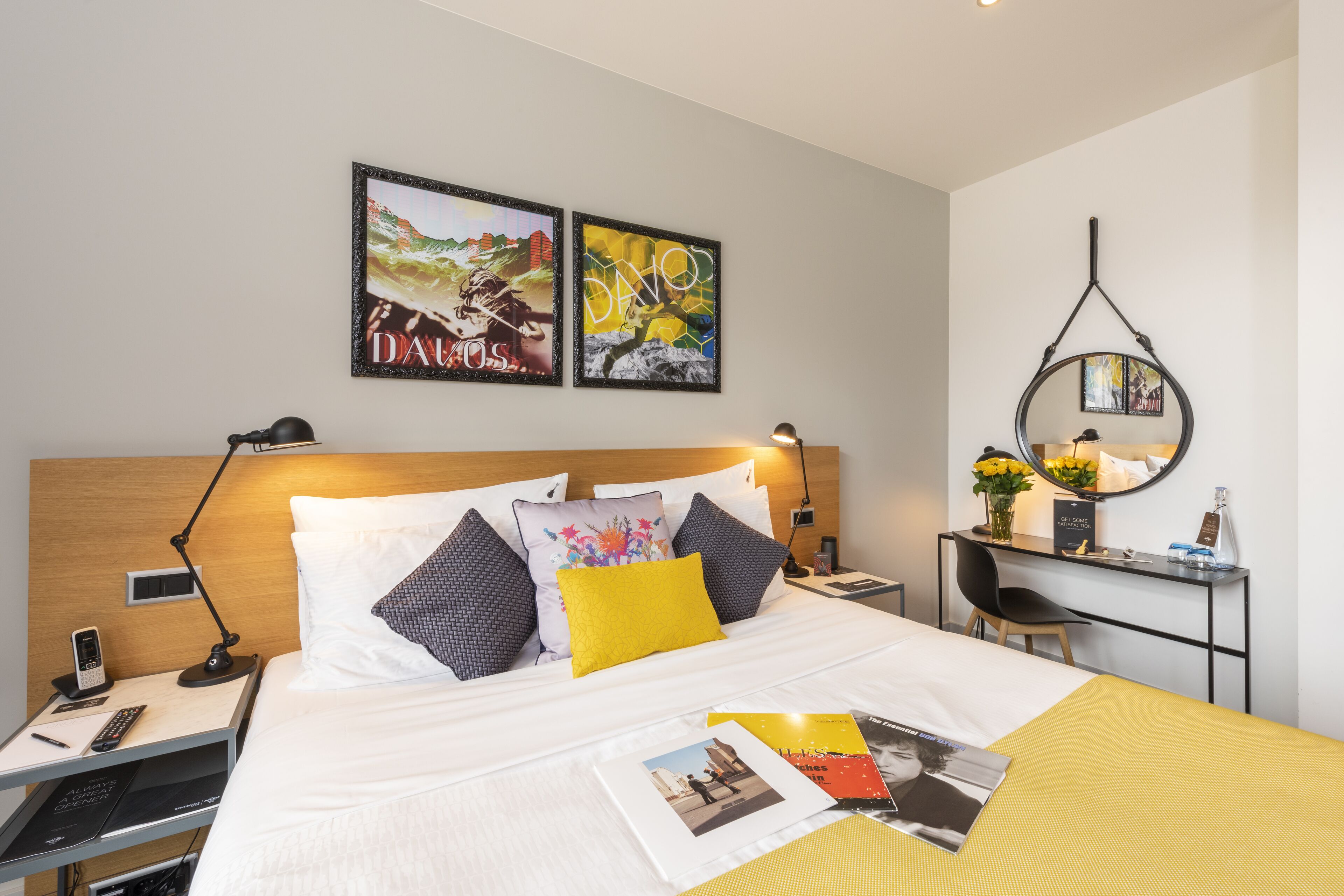 Une chambre d’hôtel avec un lit, des tables de chevet, un bureau et une chaise. Deux œuvres d’art encadrées ornent le mur, un miroir est posé sur le bureau et un téléphone se trouve sur la table de chevet.