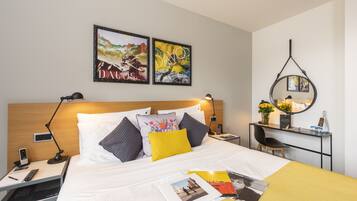 Une chambre d’hôtel avec un lit, des tables de chevet, un bureau et une chaise. Deux œuvres d’art encadrées ornent le mur, un miroir est posé sur le bureau et un téléphone se trouve sur la table de chevet.