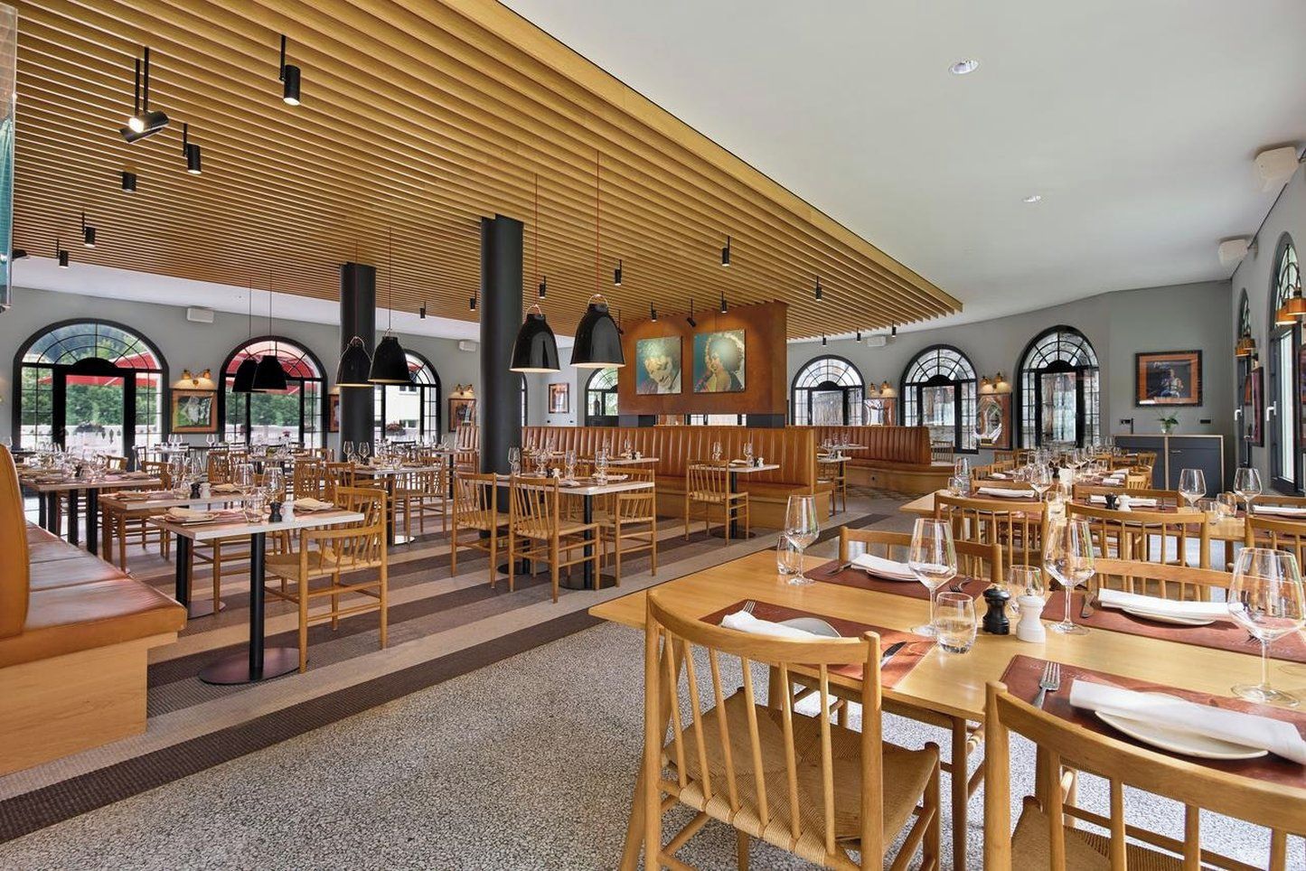 Un restaurante espacioso con varias mesas y cabinas, amplias ventanas y un alto techo con listones de madera.
