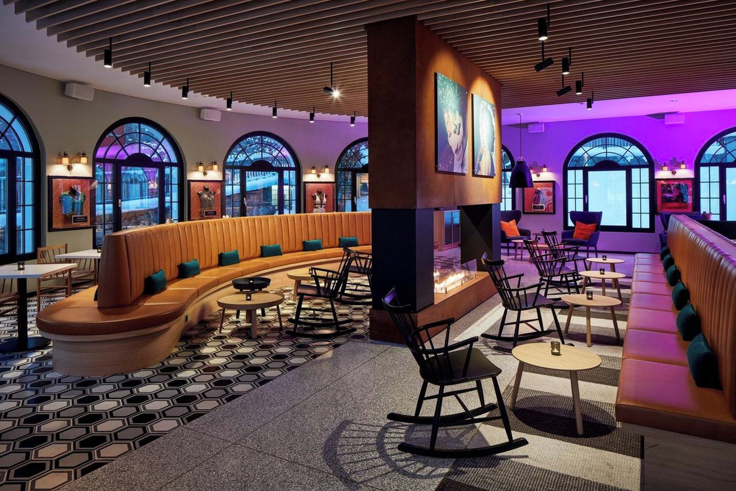 A modern lounge area with a curved seating arrangement, a central fire feature, and large arched windows.