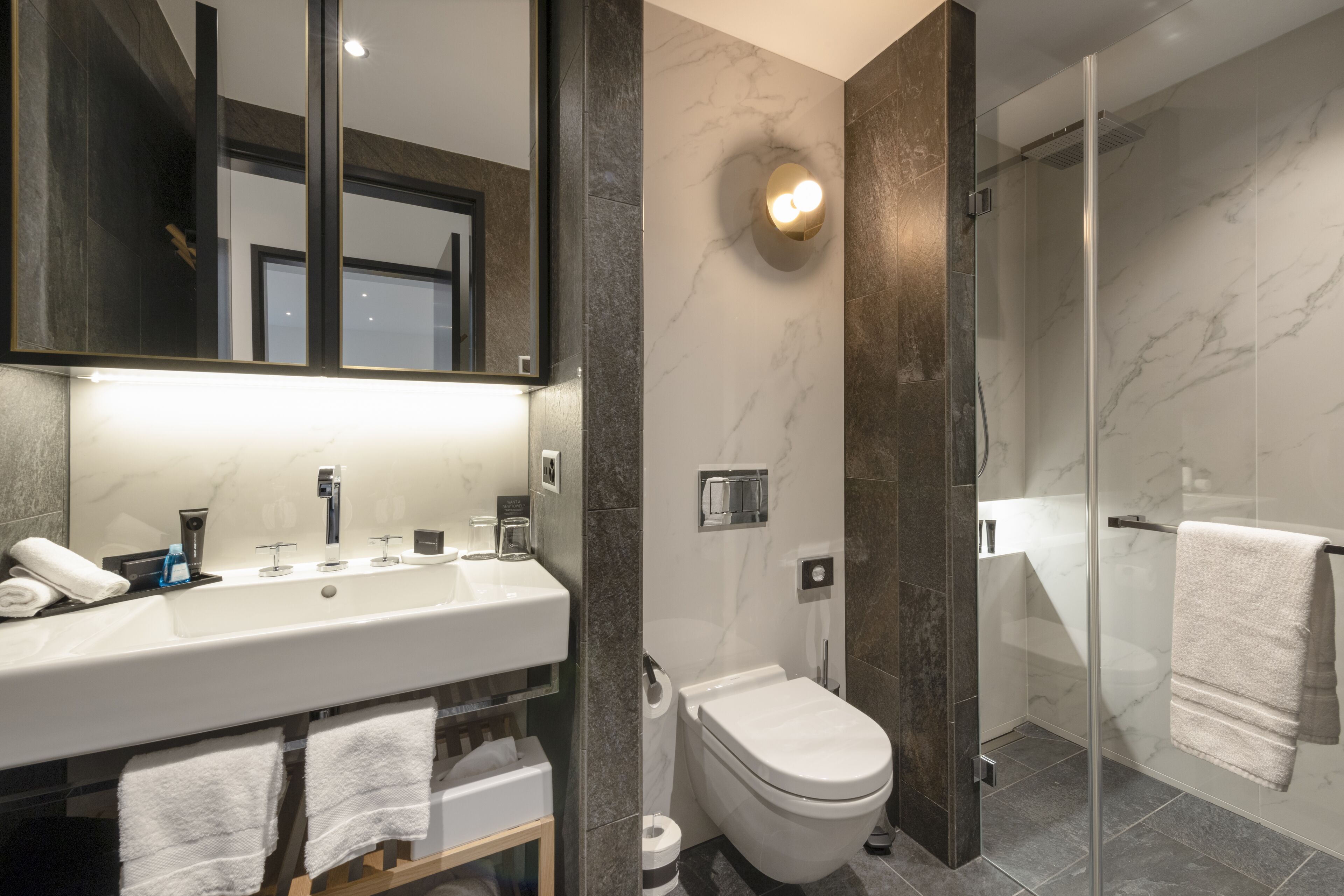 A modern bathroom with a large mirror, a sink, a toilet, and a glass-enclosed shower area.