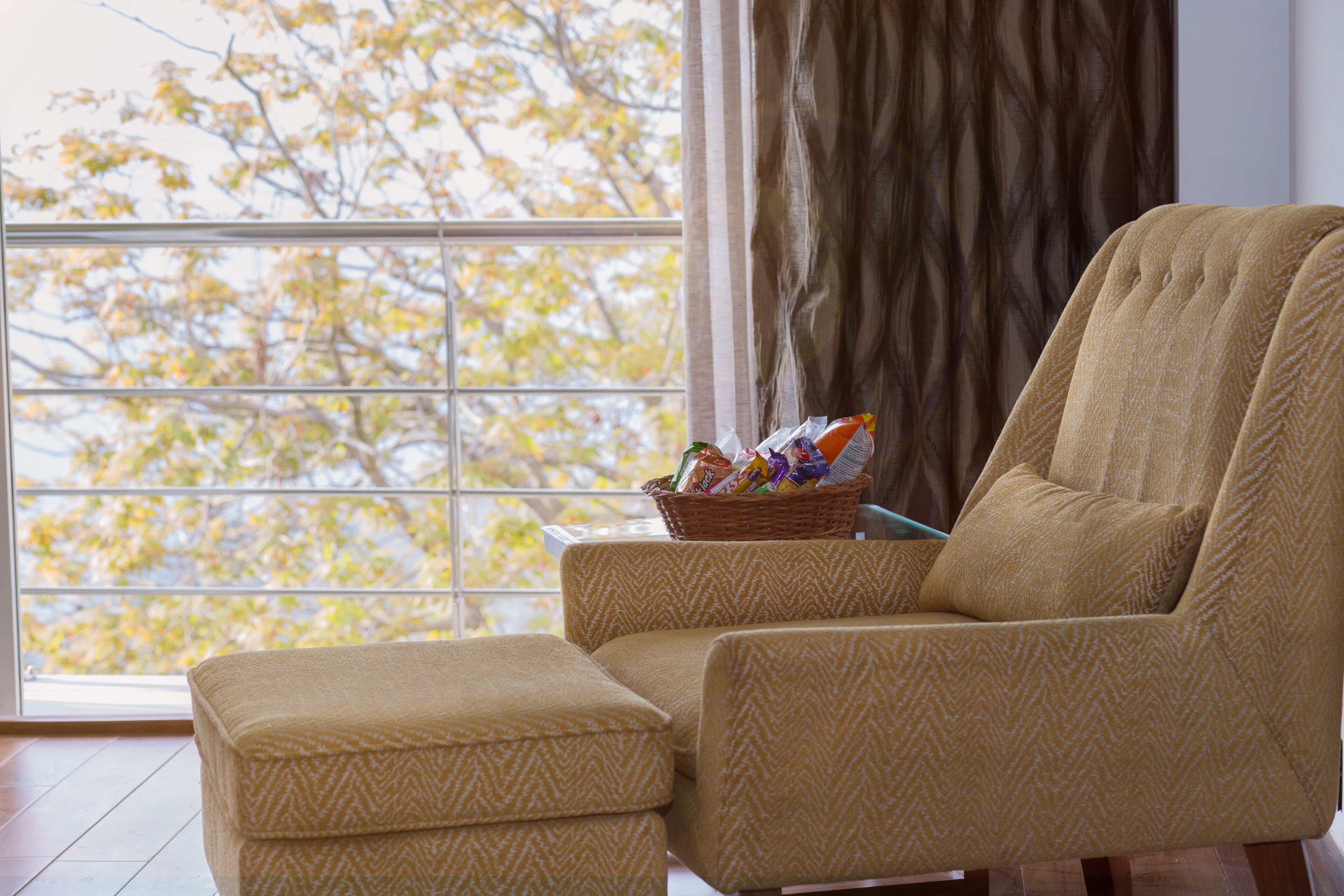 A room with a large window, a sofa, and a small ottoman.