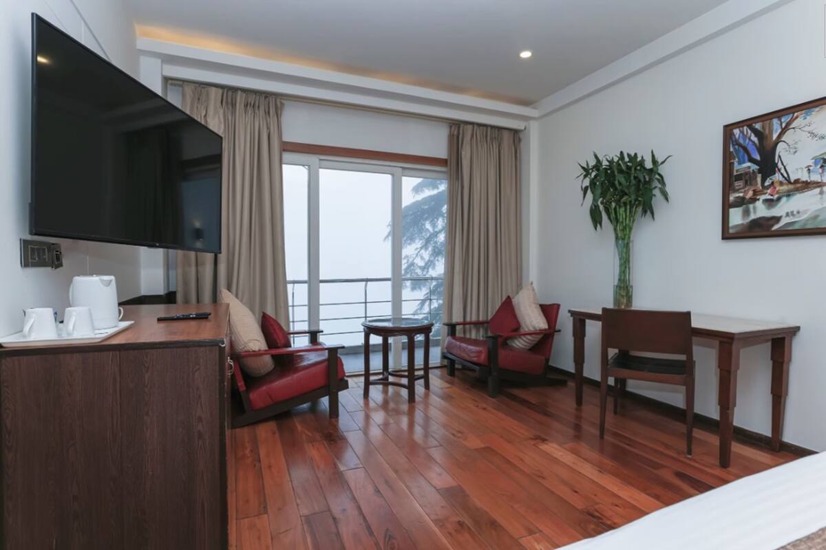 A modern hotel room with a wooden floor, a flat-screen TV, a sofa, a table, and a chair.