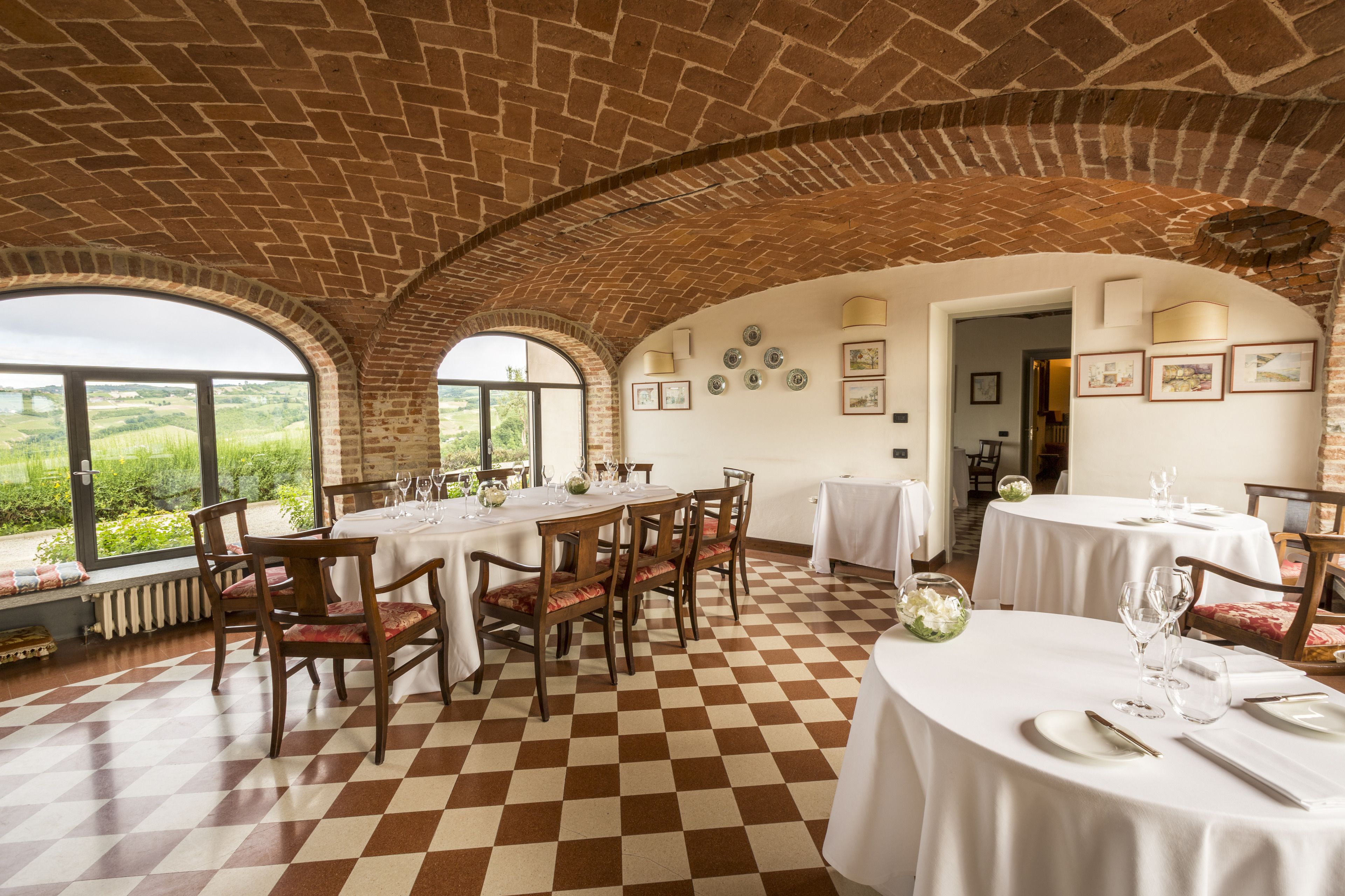 A dining area with brick arches, checkered flooring, and tables set for a meal.