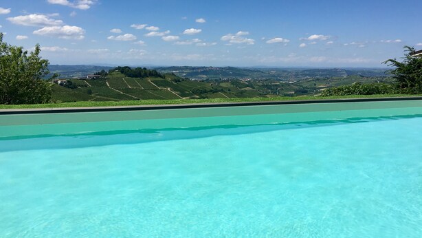 Una piscina trasparente con vista su dolci colline ed edifici in lontananza.