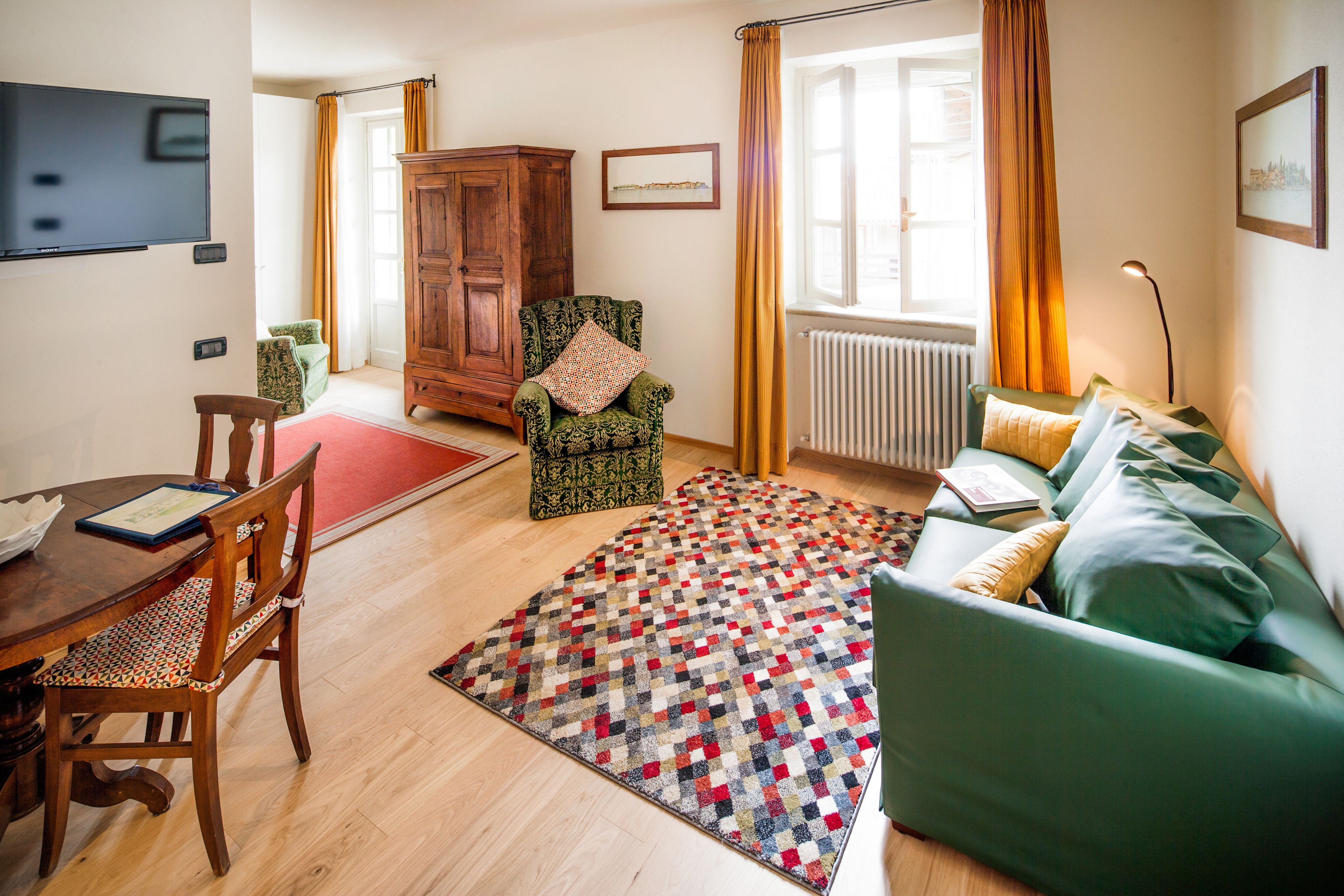 Un salon avec un canapé vert, un meuble en bois, un fauteuil à motifs, une table à manger avec des chaises et un tapis rouge.