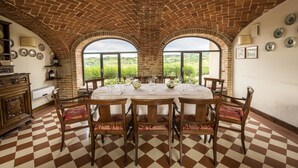 Zona pranzo con pavimento a scacchi, soffitto in mattoni e finestre ad arco che si affacciano su un paesaggio verde.