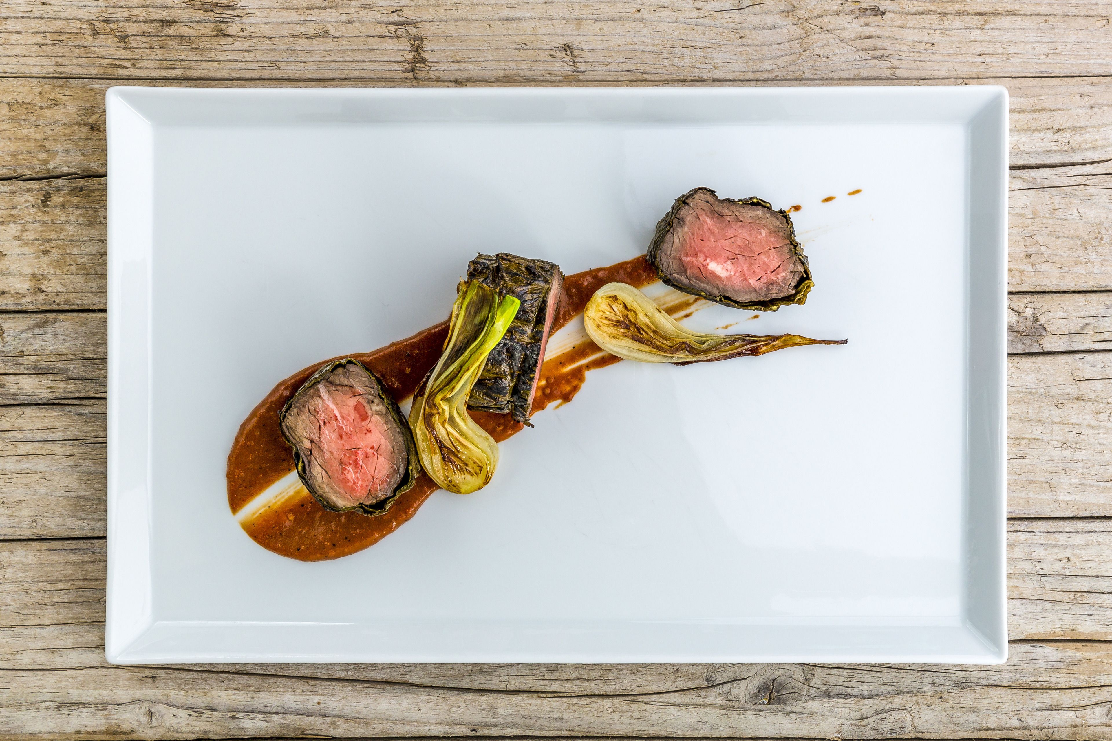 Um prato branco com bife e legumes sobre uma mesa de madeira.