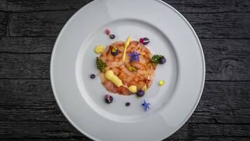 Une assiette blanche contenant un plat de fruits de mer, agrémenté d’herbes et de fleurs comestibles, posée sur une surface en bois sombre.