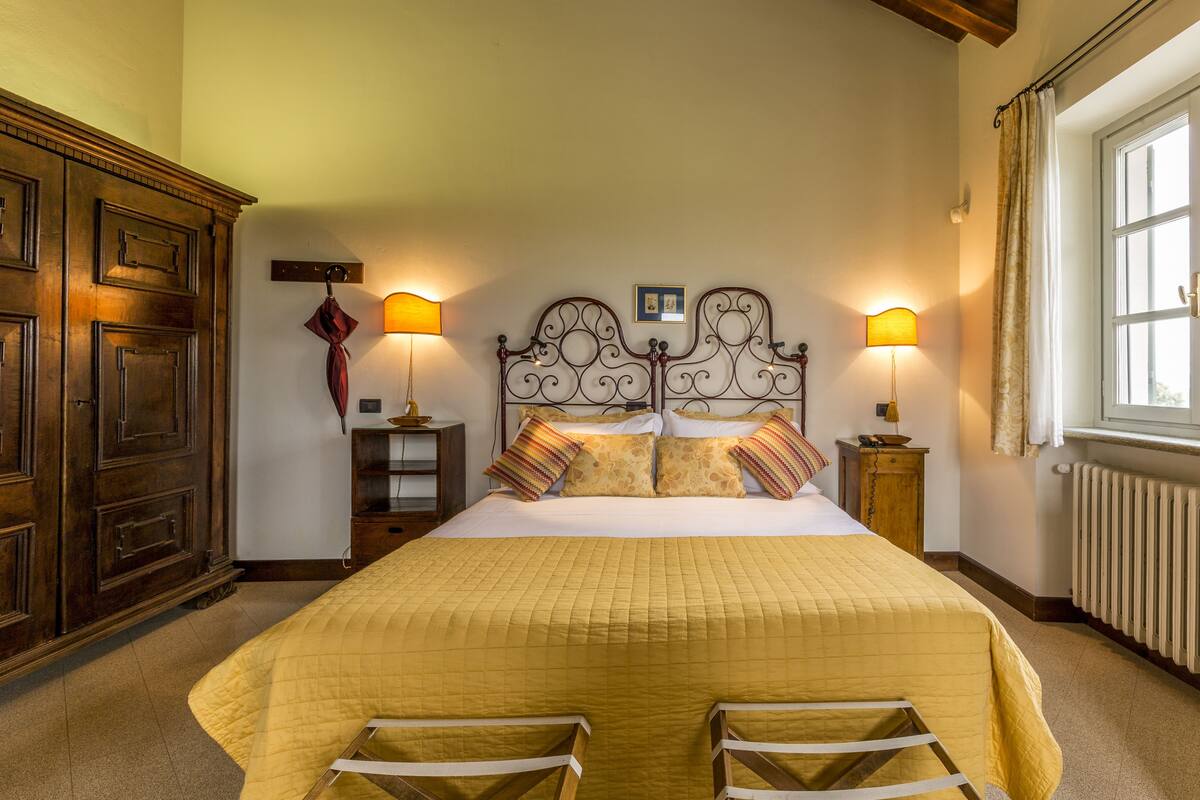 A hotel room with a large bed, two bedside lamps, a wooden wardrobe, and a window with curtains.