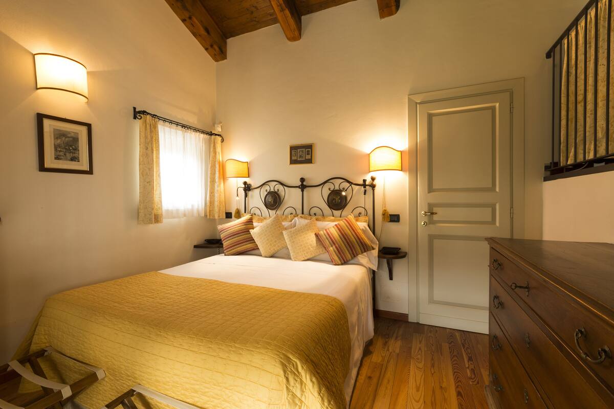 A bedroom with a bed, bedside lamps, a wooden dresser, and a door.
