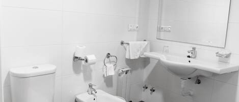 A modern bathroom with a toilet, bidet, sink, and mirror.