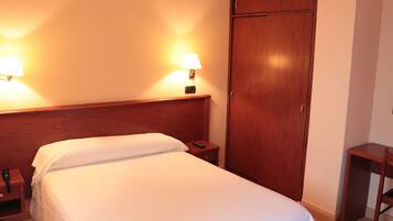 Una habitación de hotel con cama, lámparas de noche, un armario de madera y una mesita.