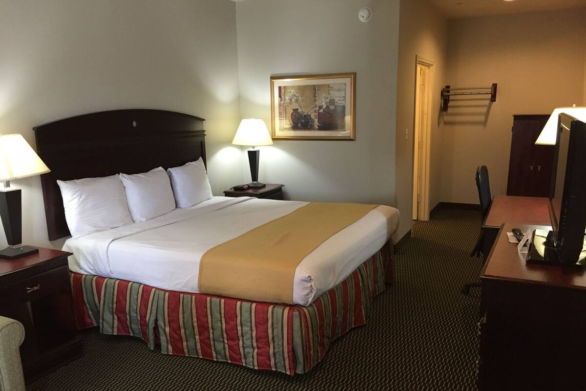 Una habitación de hotel con una cama grande, dos lámparas de noche, un escritorio con una computadora y una silla.