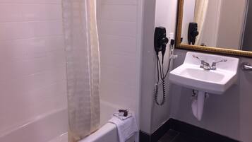 A bathroom with a white bathtub, a white sink with a gold-framed mirror, and a hairdryer on the wall.