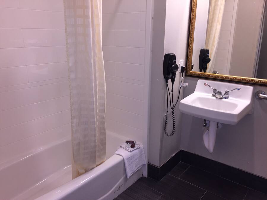 A bathroom with a white bathtub, a white sink with a gold-framed mirror, and a hairdryer on the wall.