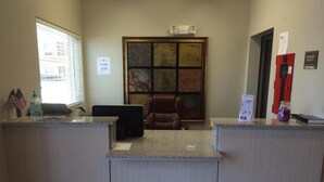 A reception area with a desk, a computer, a chair, and a window with blinds. There is a sign indicating a $1.00 charge for drinks. - Express Inn (Wharton)