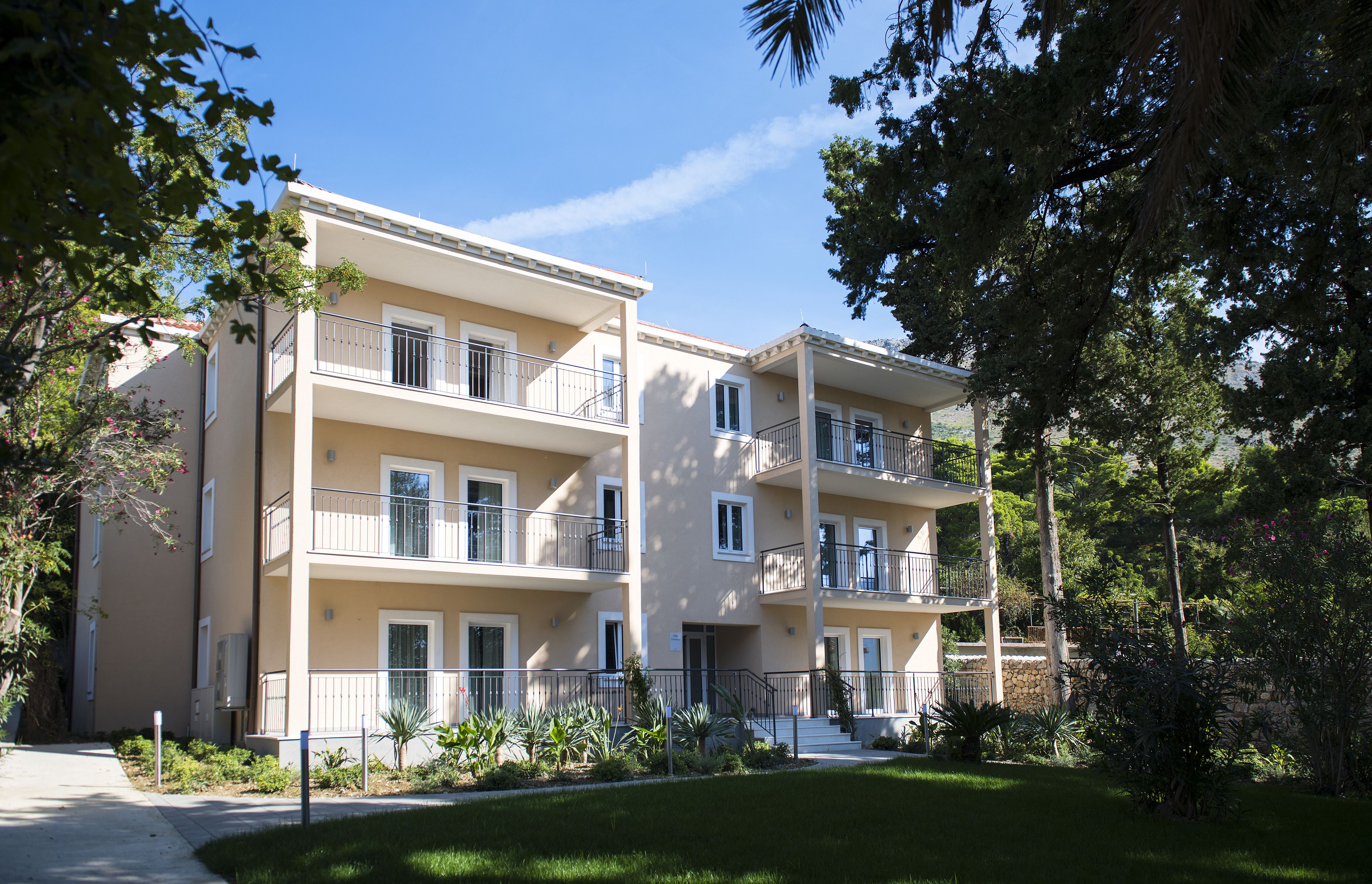 A multi-story residential building with balconies, a paved driveway, and surrounding greenery.