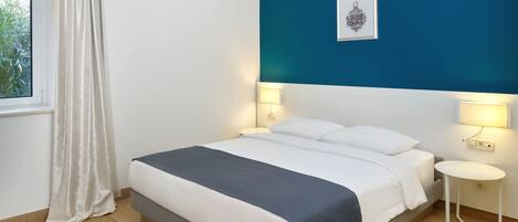 A bedroom with a bed, bedside lamps, a window with curtains, and a blue accent wall.