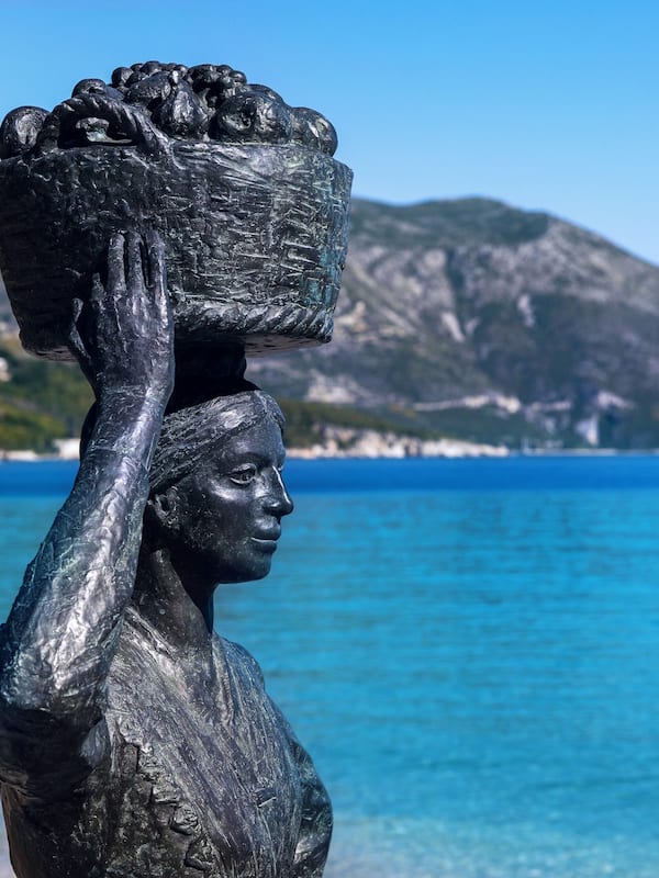 Statue stands on a beach overlooking a mountainous landscape and the sea.