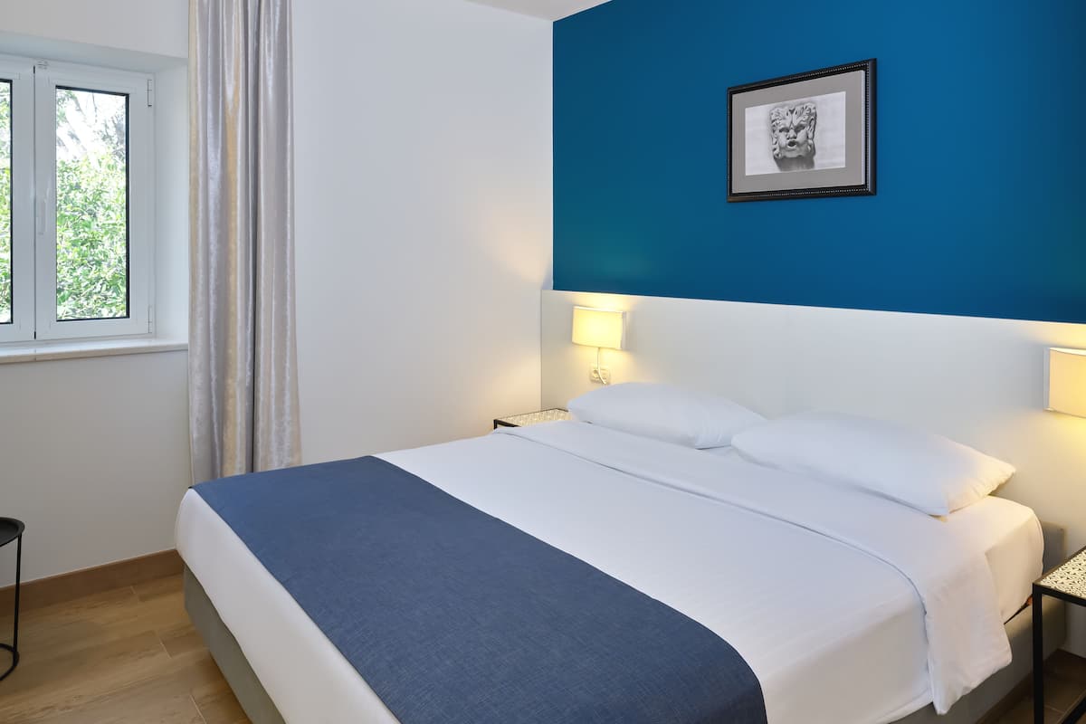 Een netjes opgemaakt bed met witte lakens en een blauw accent, een bedlampje en een ingelijste foto aan de muur.