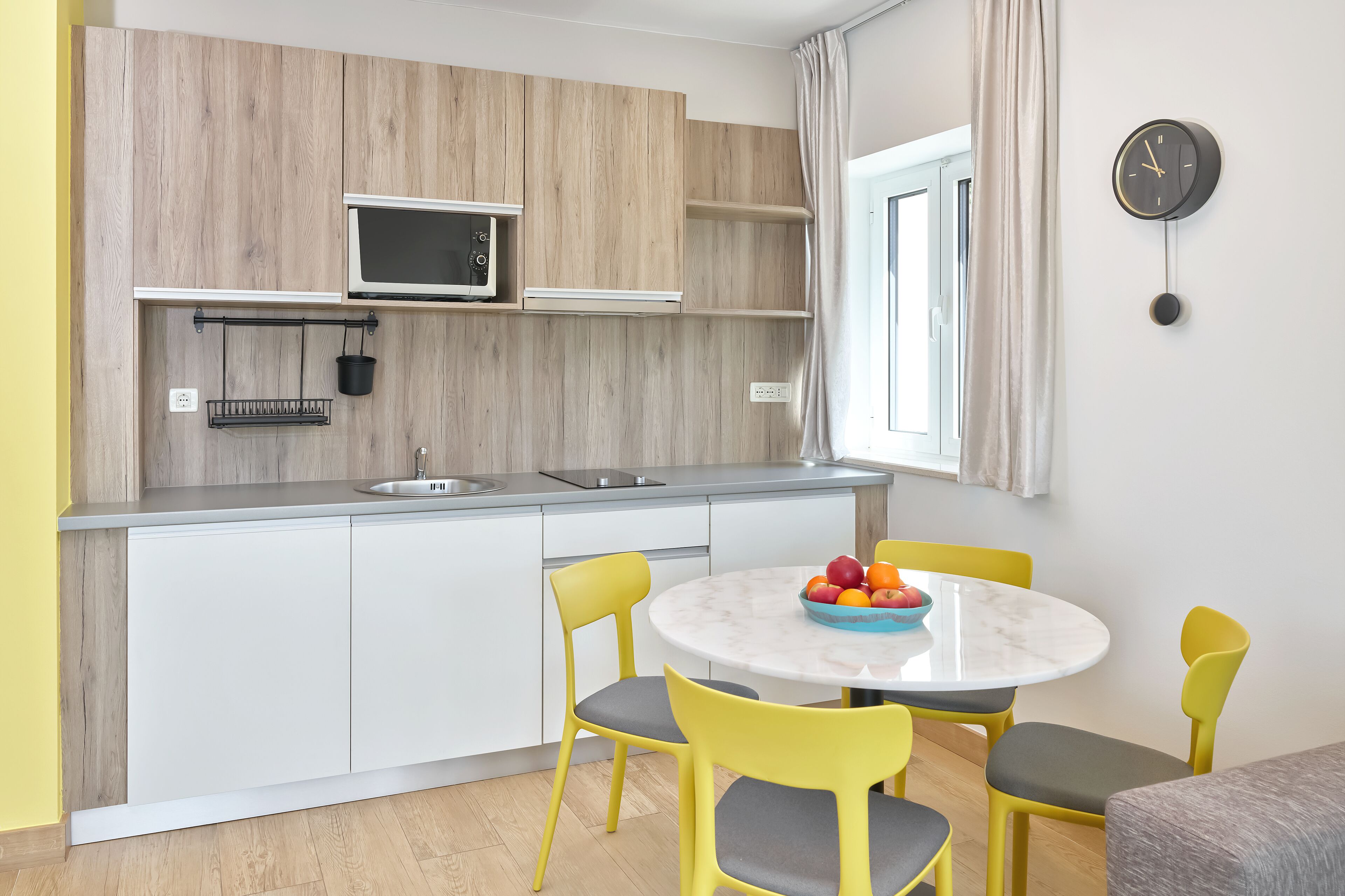 A compact kitchen with a microwave, sink, and a dining area with a round table and yellow chairs.